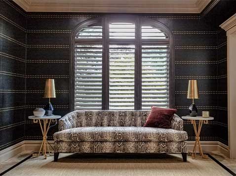 An upscale living room with a large window covered by shutter blinds