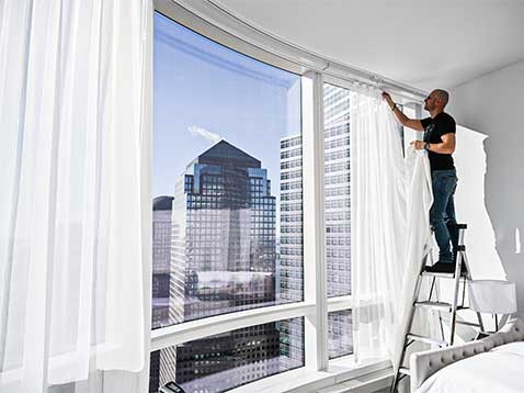 A man on a stepladder putting up white drapes